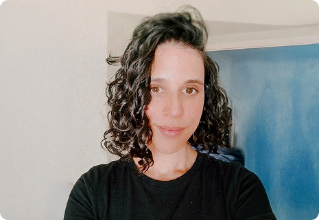 Laura smiling inside, blue art in background, curly dark hair